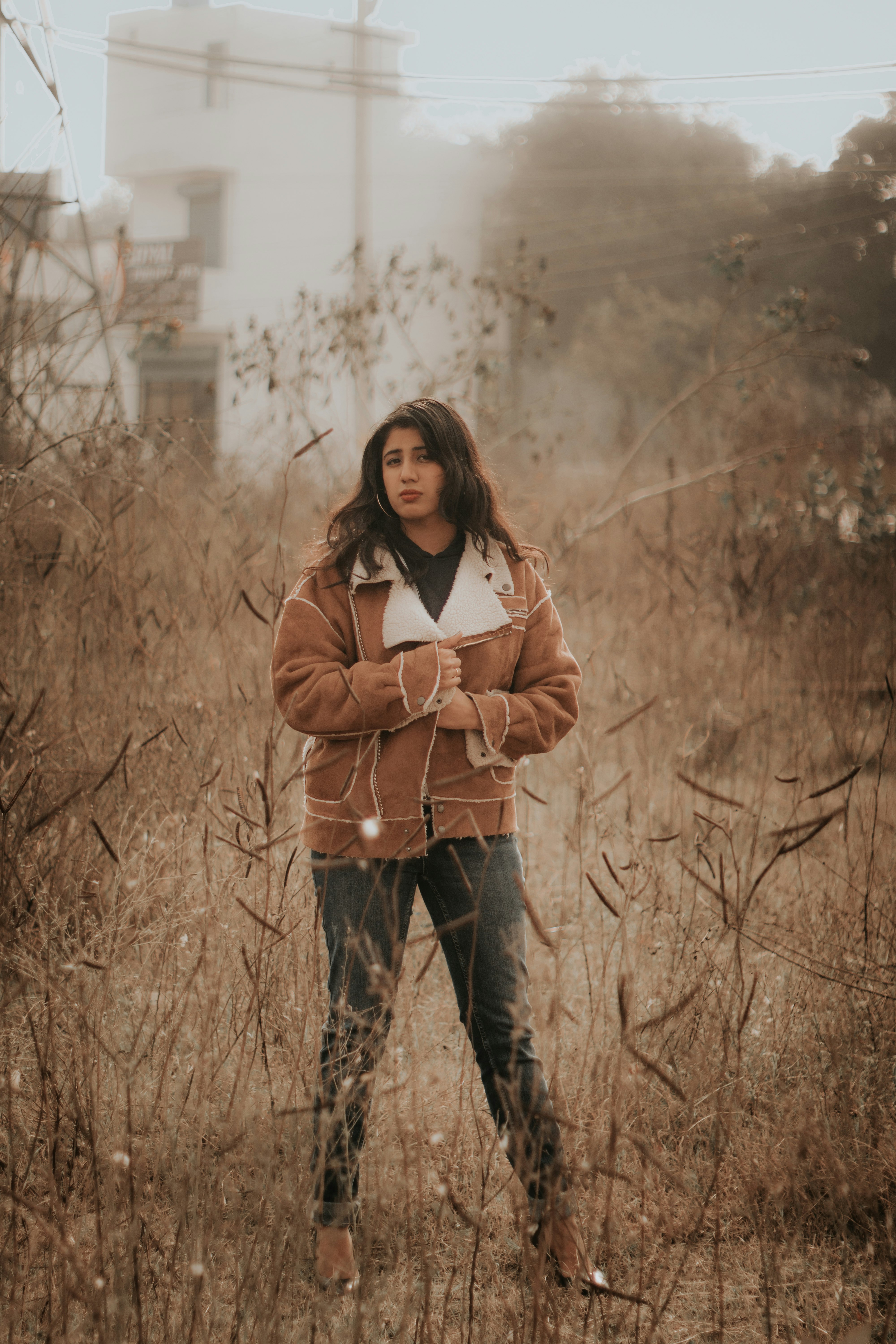 woman in brown coat standing on brown grass field